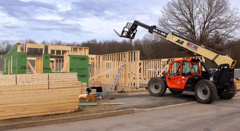 "Construction machine lifting wood-framed wall for installation at new home build site."