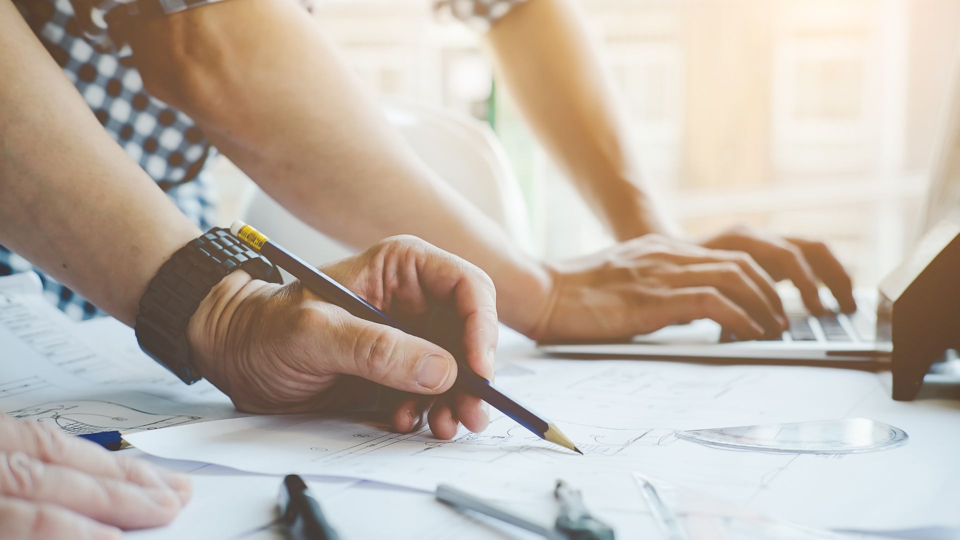 "Hands using tools to build with a blueprint on a construction project table."